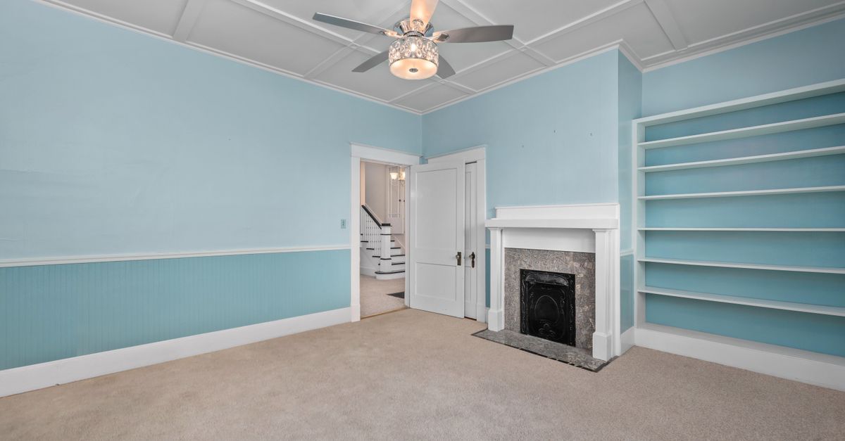 Spacious empty room featuring a classic fireplace, built-in shelves, and modern ceiling fan.