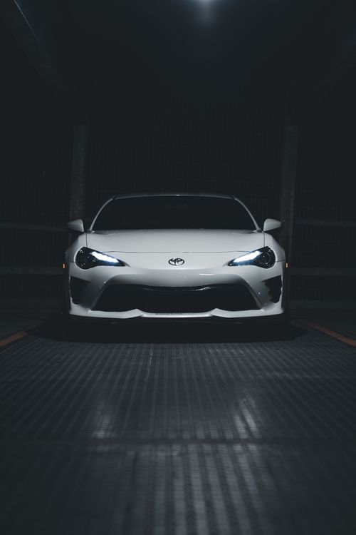 Free A white sports car with illuminated headlights in a dimly lit garage at night, showcasing elegance and power. Stock Photo