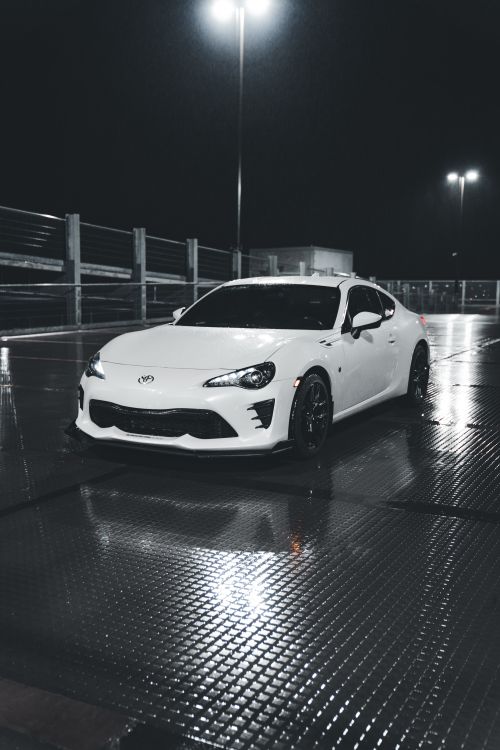 Free A white Toyota sports car parked at night on a wet rooftop, reflecting the urban lights. Stock Photo