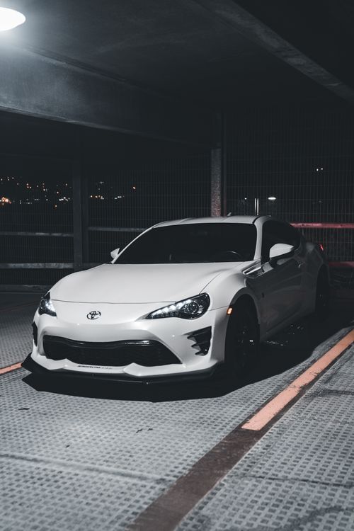 Free White Toyota car parked in an urban parking garage at night. Moody lighting enhances the sleek design. Stock Photo