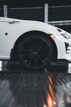 Close-up of a sleek white car's wheel at night with reflective wet surface.