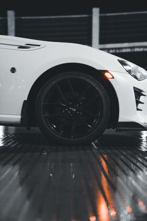 Free Close-up of a sleek white car's wheel at night with reflective wet surface. Stock Photo
