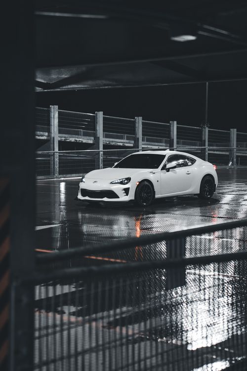 Free A modern white sports car parked on a wet city street at night, reflecting a contemporary urban vibe. Stock Photo