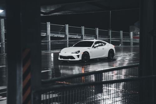 Free A stylish white car parked in an urban garage at night, reflecting on wet pavement. Stock Photo