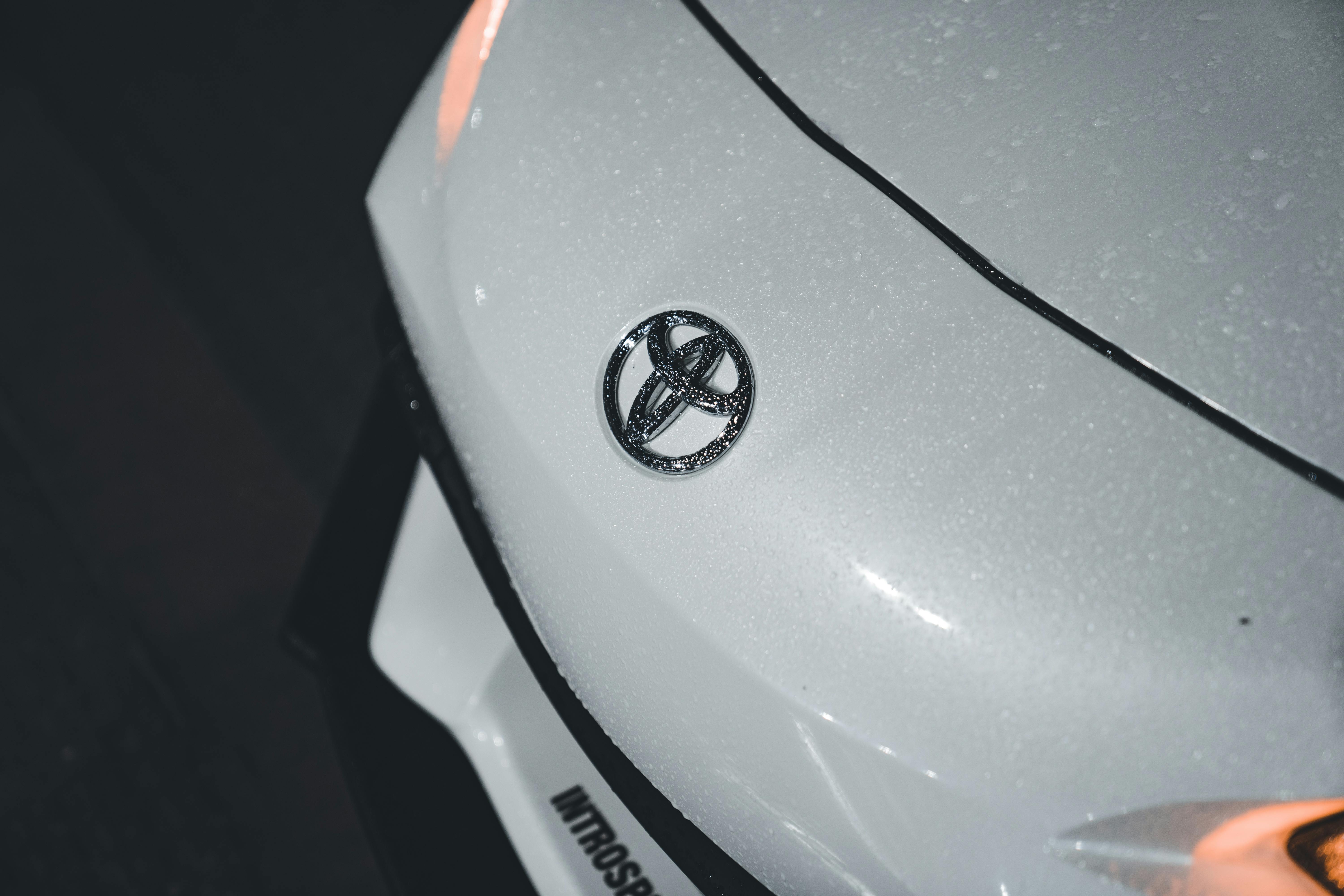 Free Detailed shot of a wet white car bonnet featuring the Toyota logo, highlighting texture and shine. Stock Photo