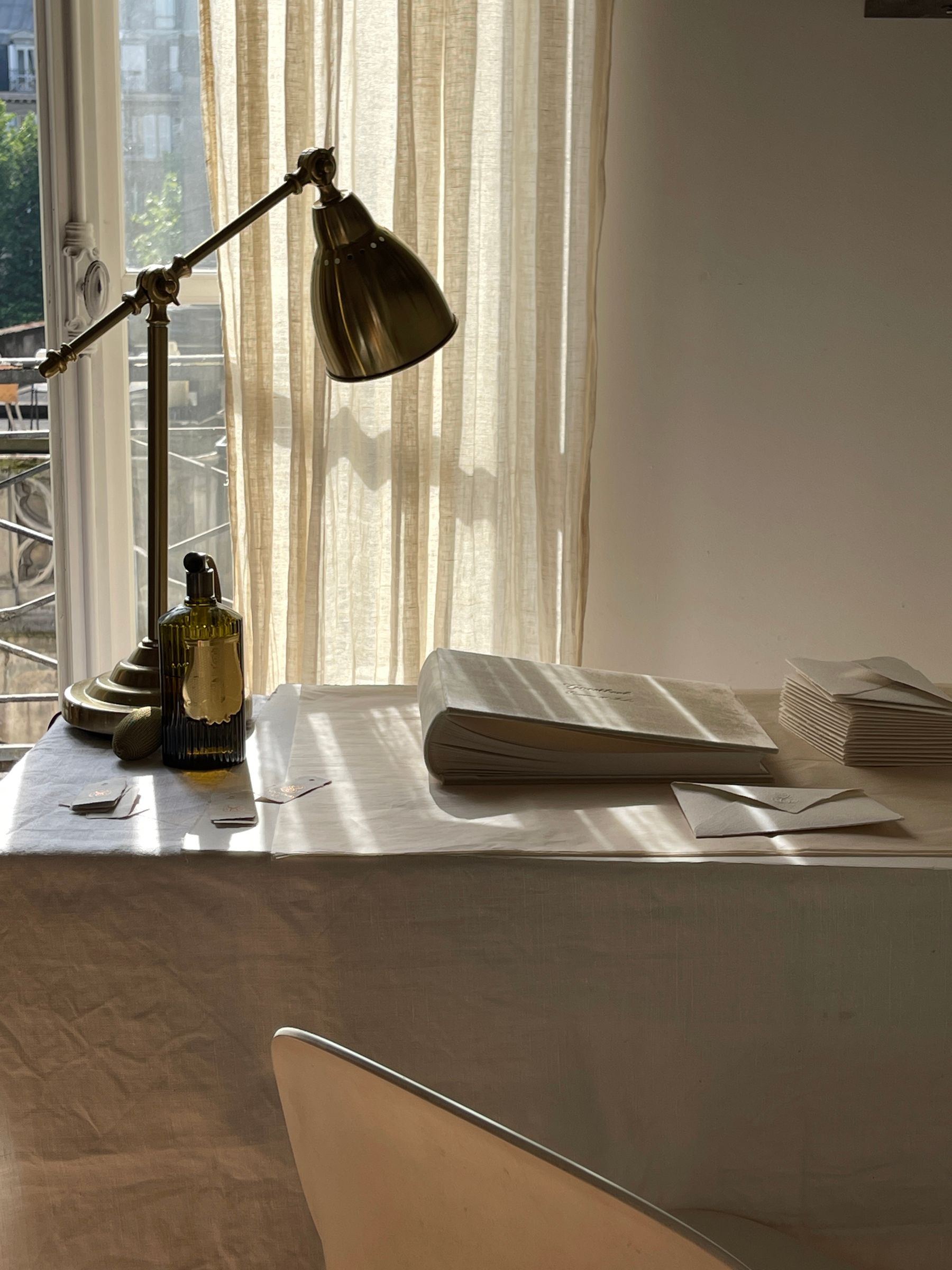 Articulated warm metal desk lamp beside a window with sheer curtains, papers and an open book