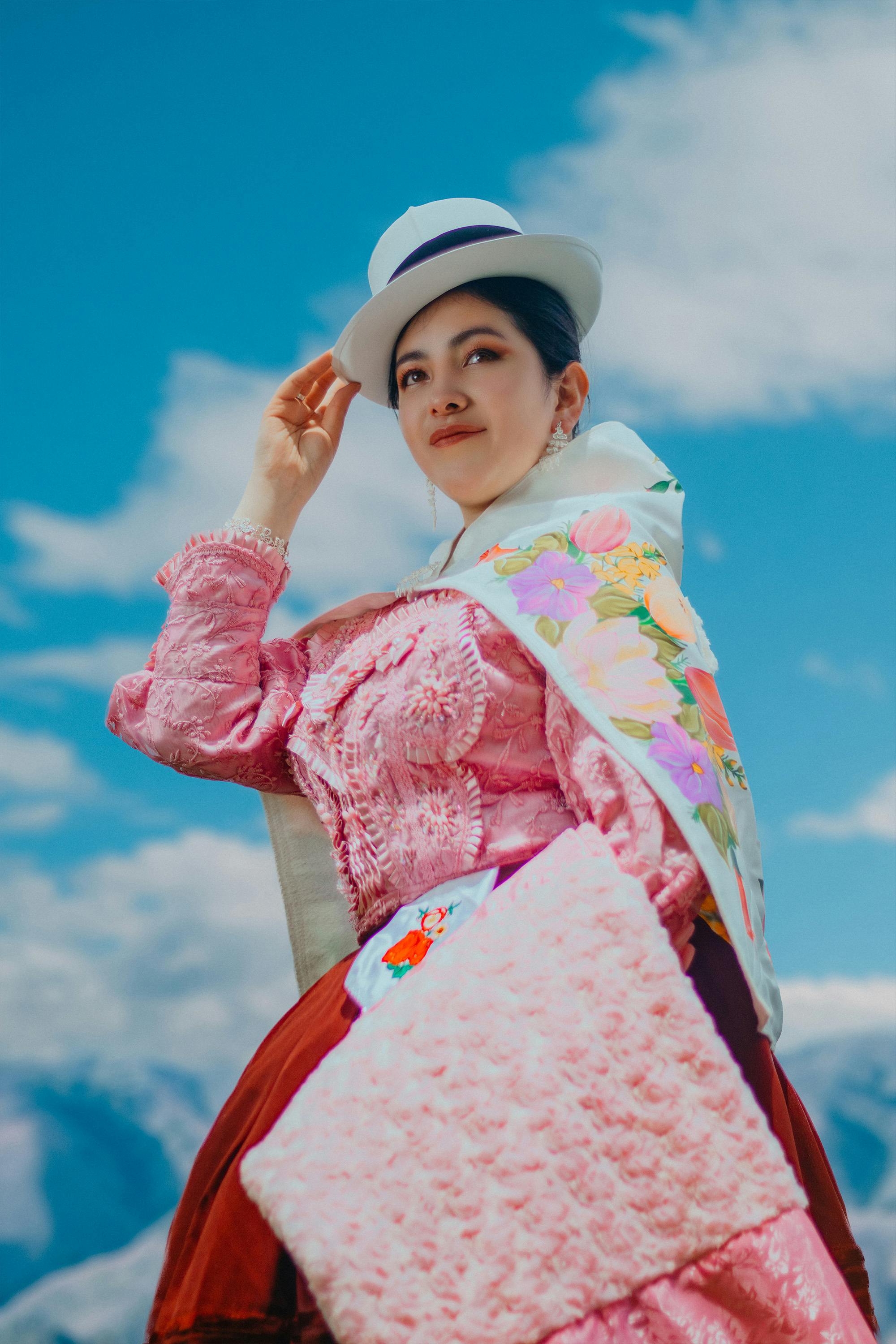 Woman in vibrant Andean attire poses against a clear blue sky, showcasing Peruvian culture.