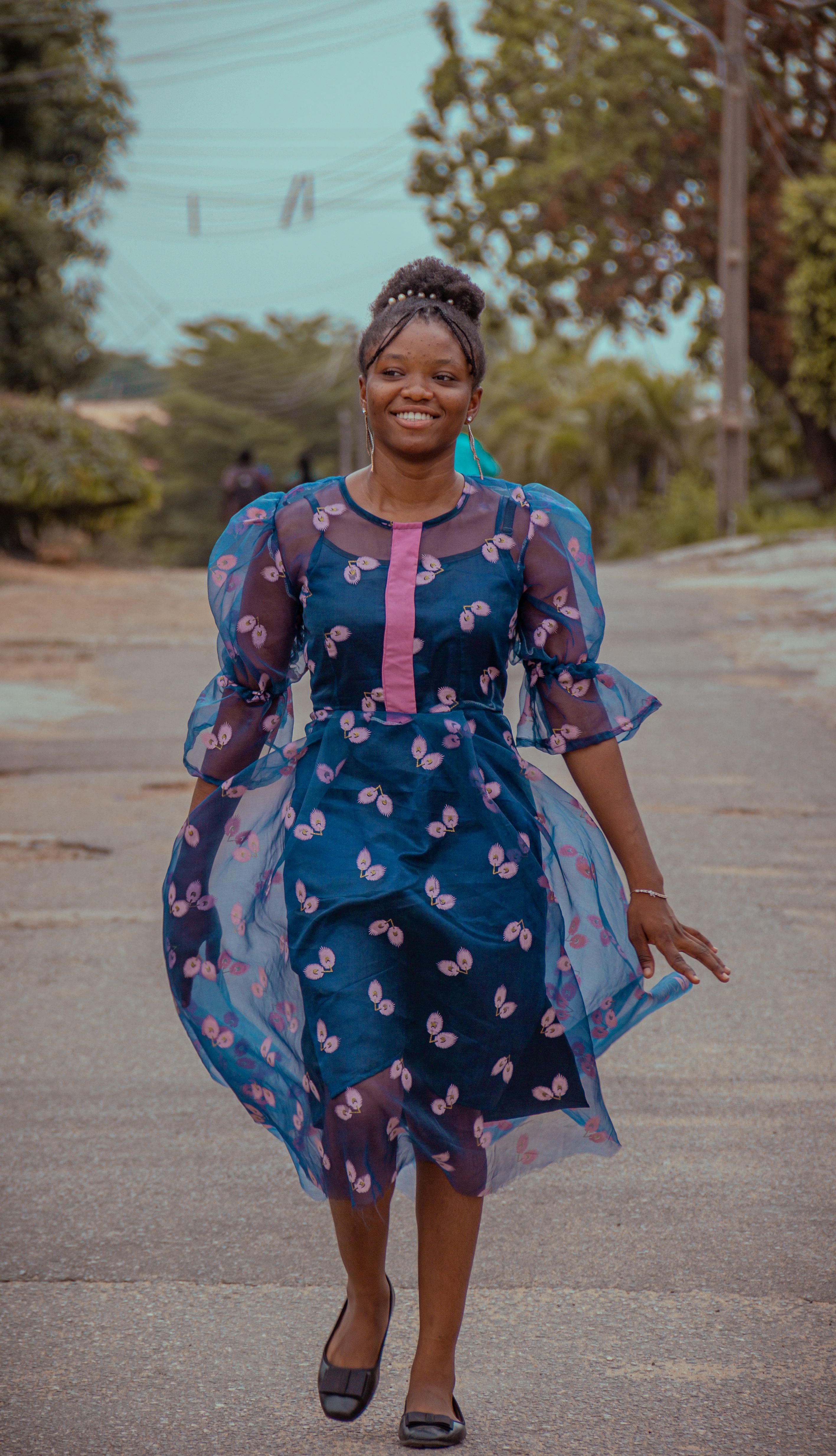 Smiling woman in a patterned blue dress walking outdoors in Nigeria.
