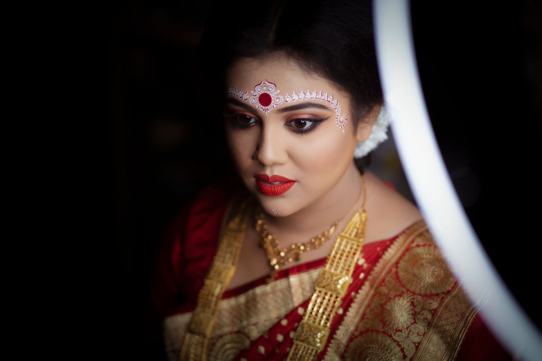 Portrait of an Indian bride in Kolkata wearing traditional red and gold sari with intricate makeup.
