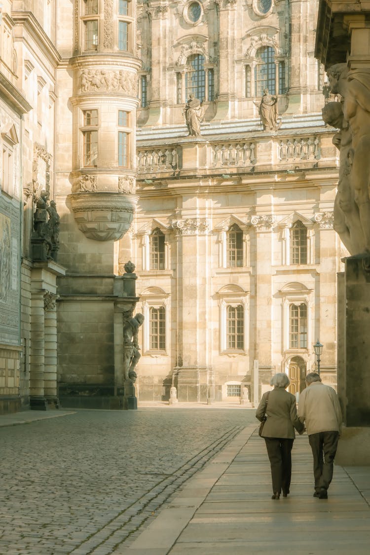 Elderly Man And Woman Walking Towards Ornamented Cathedral Wall