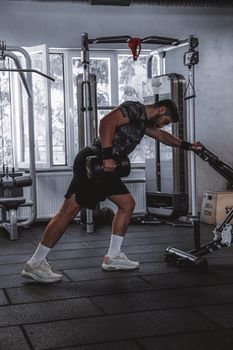 Muscular man performing dumbbell row exercise in a contemporary gym.