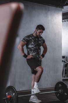 Adult male athlete resting in a gym after lifting weights with a barbell. Indoor fitness lifestyle scene.