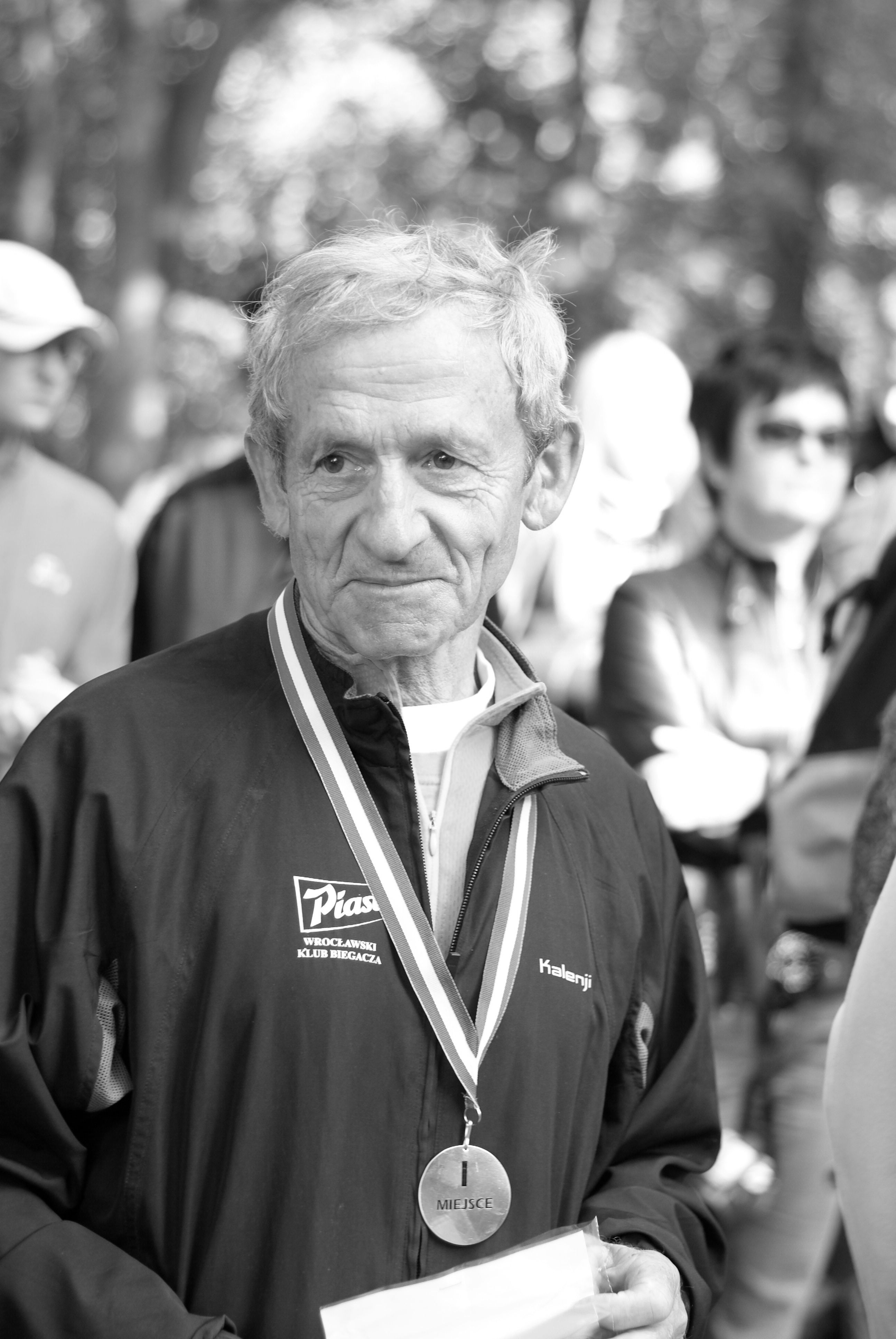 Black and white portrait of a senior athlete proudly wearing a medal outdoors.
