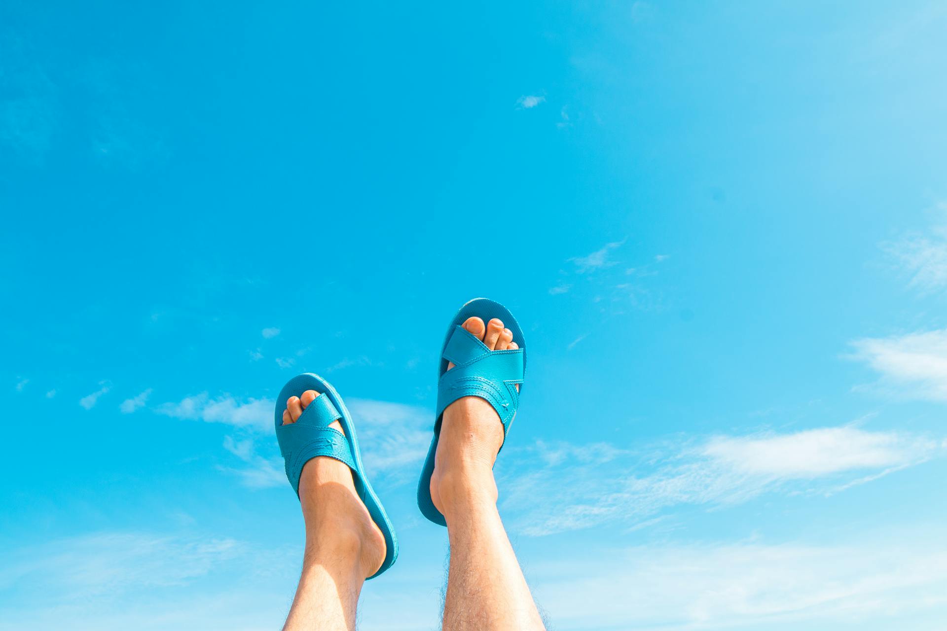 Feet in blue sandals against a clear summer sky, embodying relaxation.