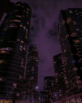 Dark cityscape featuring illuminated skyscrapers and clouds at night.
