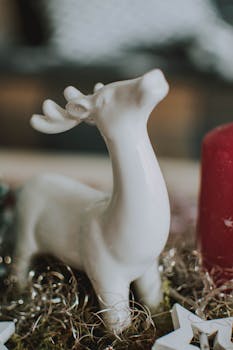 一尊白色陶瓷鹿雕像，装饰着节日饰品和红色蜡烛