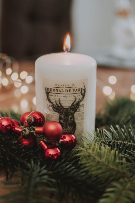 Close-up of a white candle with red ornaments and pine branches, evoking holiday warmth.