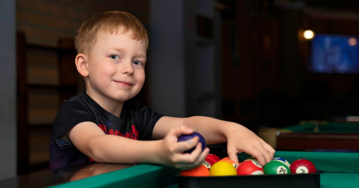 A child joyfully preparing to play pool indoors, showcasing a playful and fun atmosphere.
