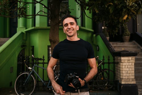 Man Holding Camera Standing in front of Green House