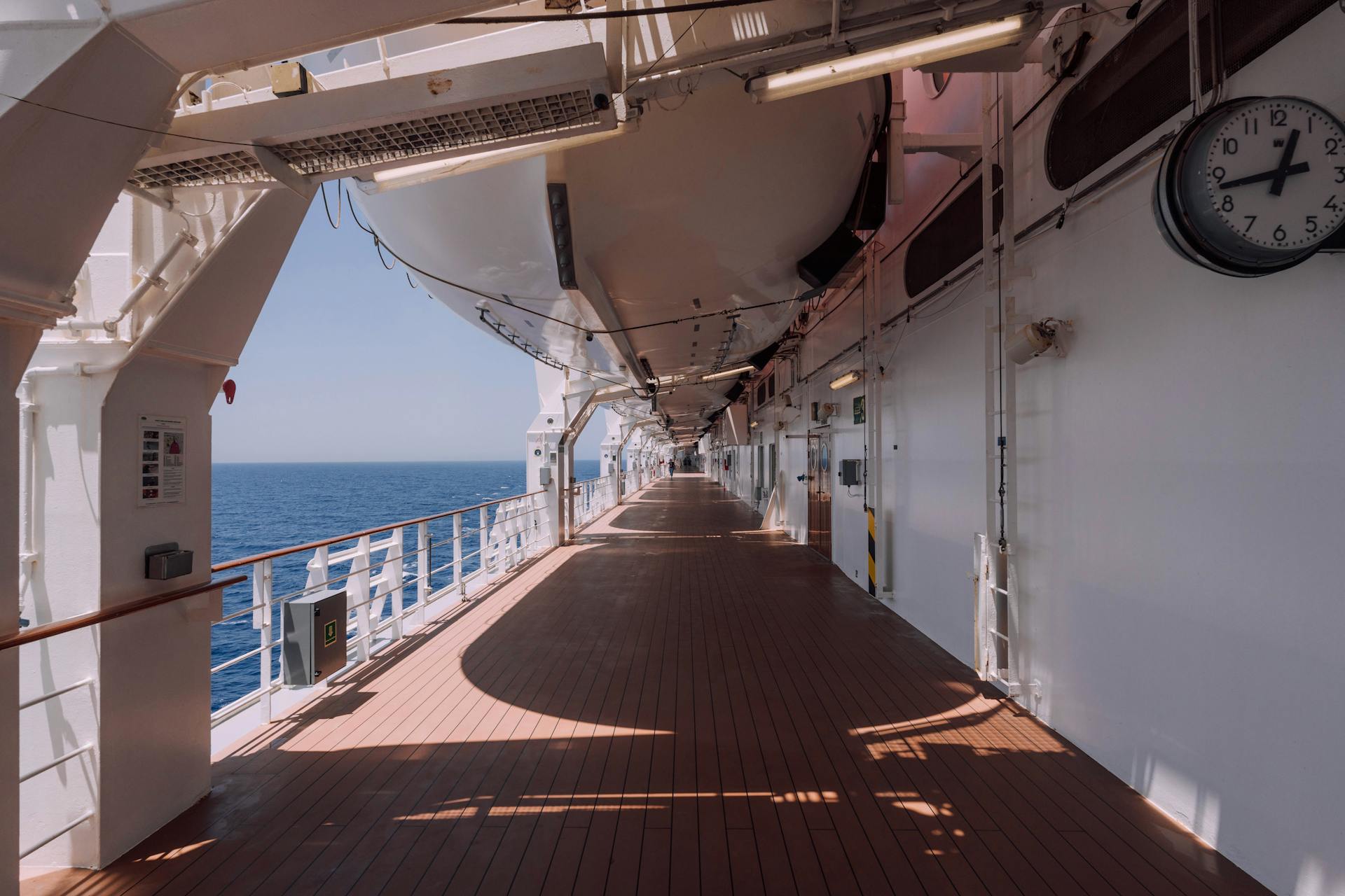 Wide view of an empty cruise ship promenade deck with ocean view and shadows.