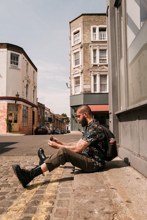 Man Sitting on Cobblestone Street Taking Photo