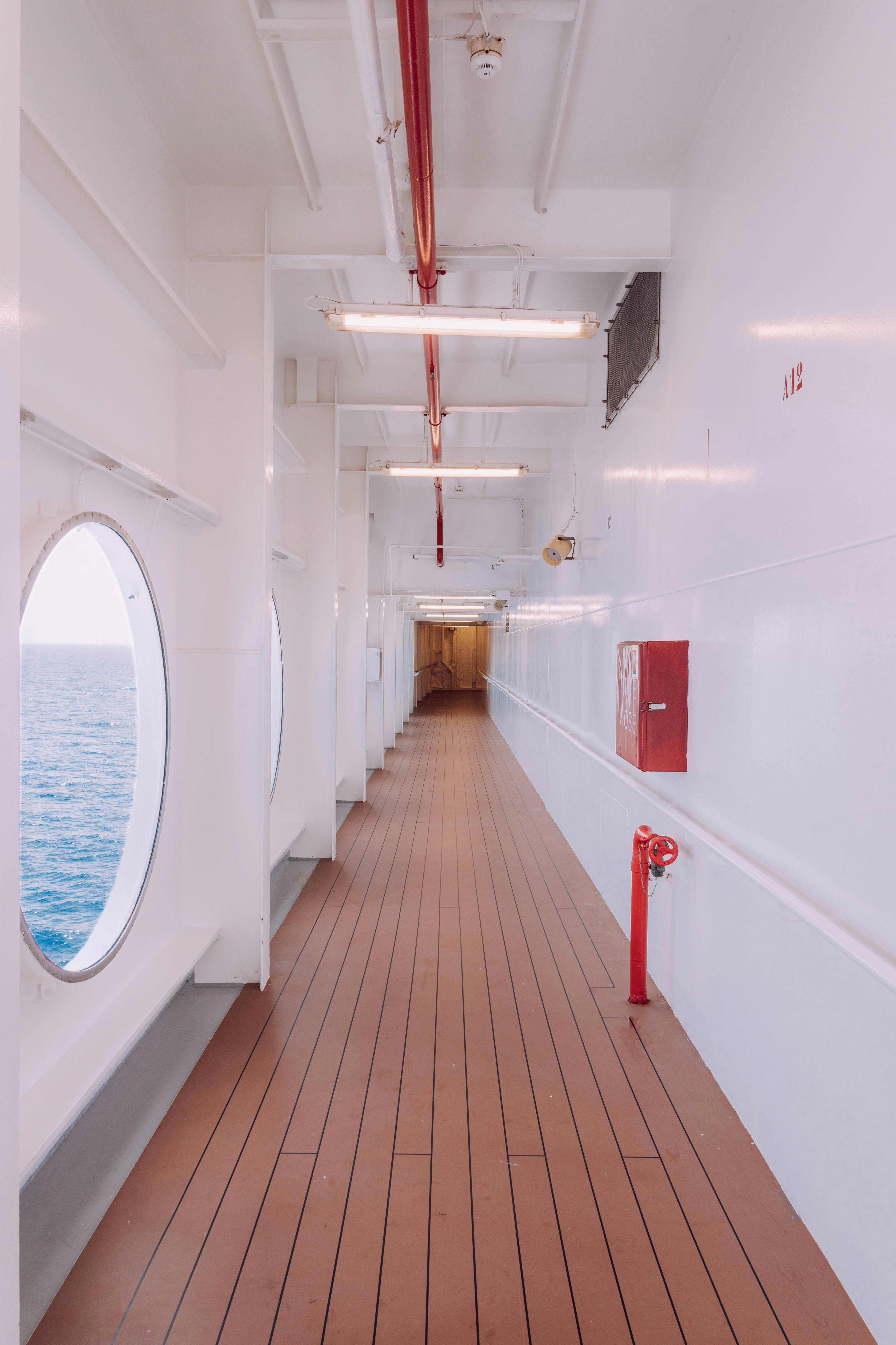 Wide shot of a ship's corridor with wooden flooring, portholes, and ocean view, offering tranquil travel vibes.
