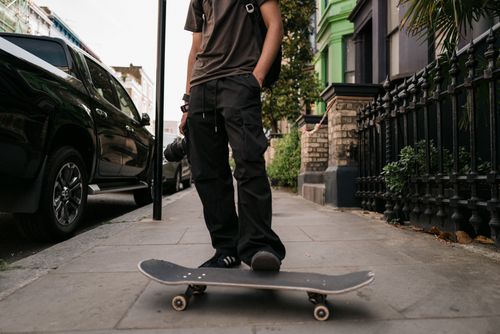 Free Young man with a skateboard stands on a London sidewalk, camera in hand. Stock Photo
