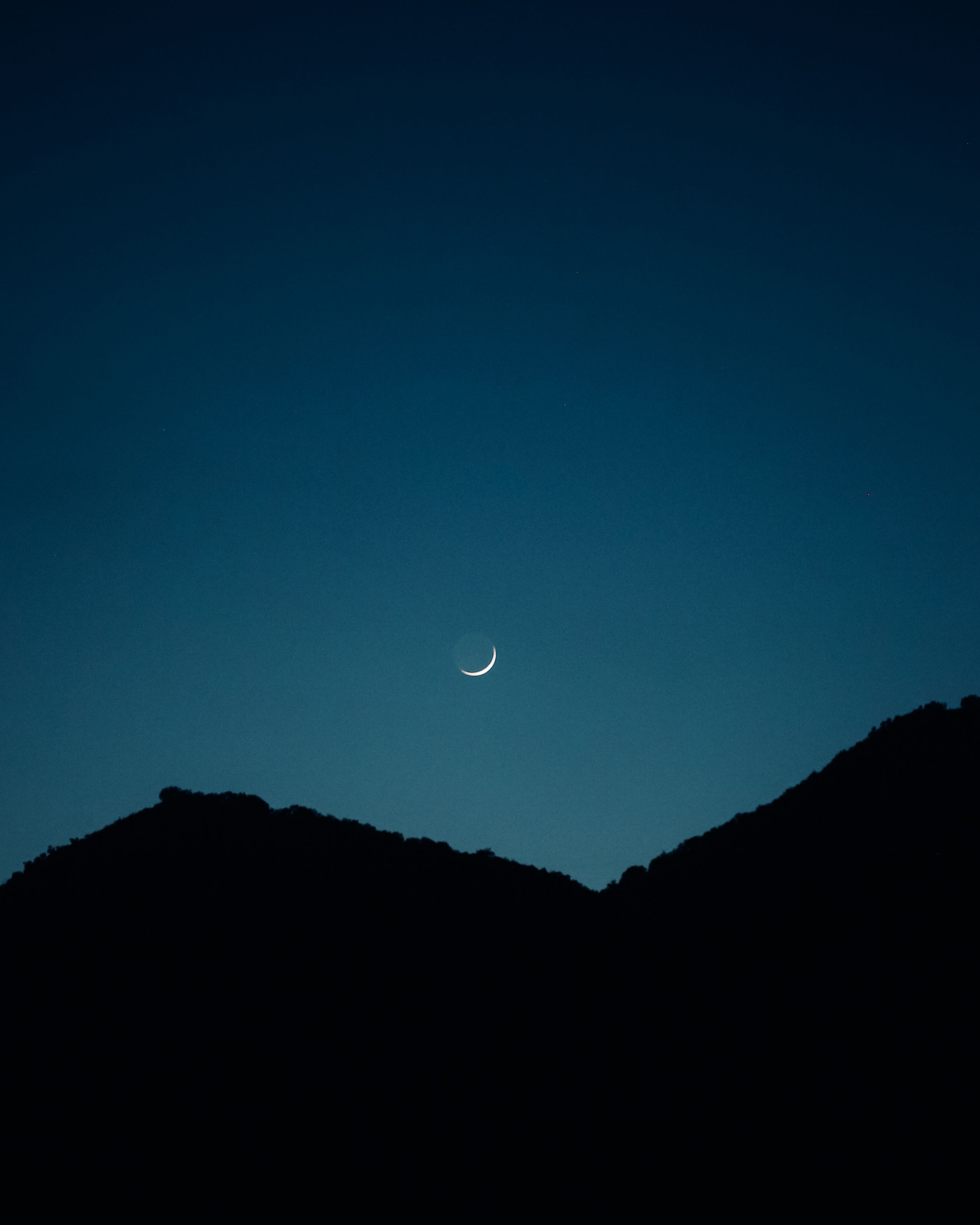 A serene crescent moon above the silhouette of Tivat mountains under a clear night sky.