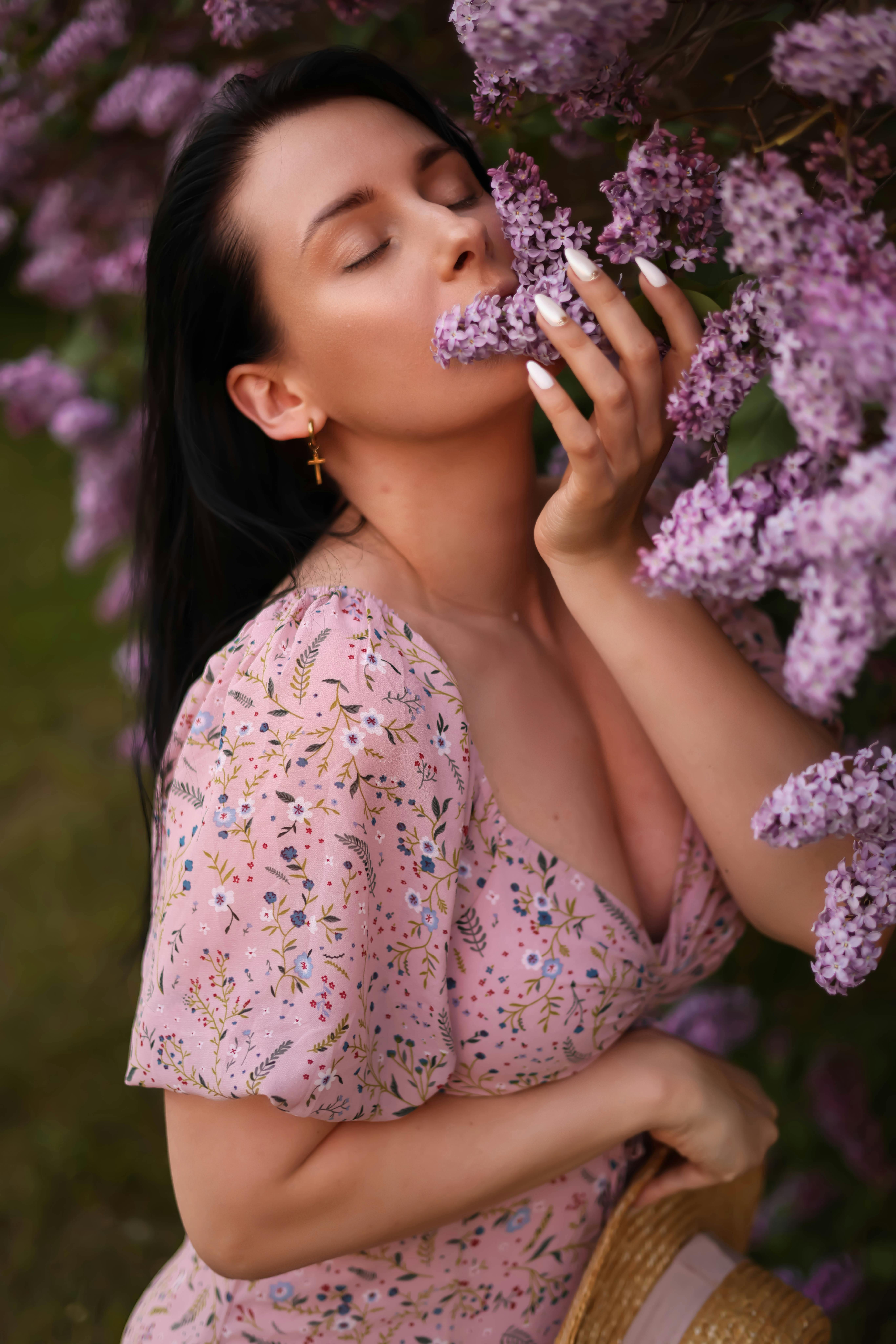 Portrait of a woman in pink dress enjoying fragrant lilacs in a lush summer garden.