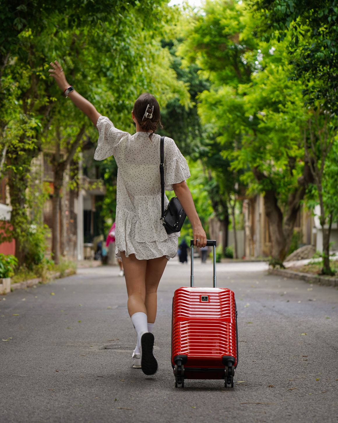 A traveller walking down a tree-lined street pulling a cabin suitcase. Photo by Soner Ozcan on Pexels.
