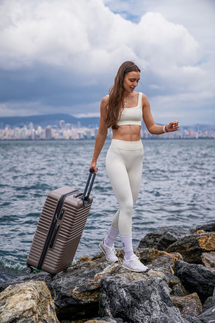 Woman Walking On The Rocky Coastline With A Suitcase 