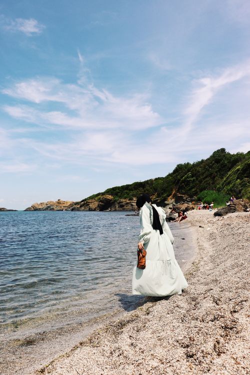 Free Woman in a flowing dress walking along a beautiful beach, capturing elegance and tranquility. Stock Photo