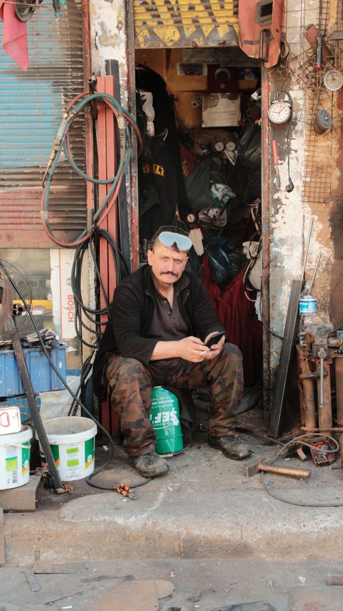 Free A man in goggles sitting in an urban workshop doorway with tools around him. Stock Photo