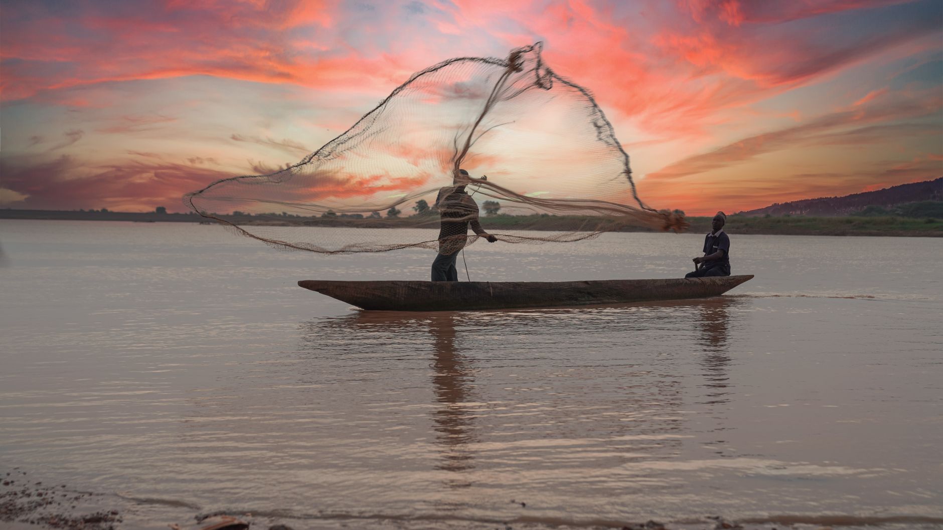 Two fishermen casting nets from a boat on a calm river during a serene sunset in Calabria, Italy.
