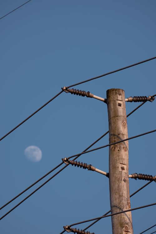 Free Wooden power pole against a clear blue sky with visible moon, showcasing electrical distribution. Stock Photo