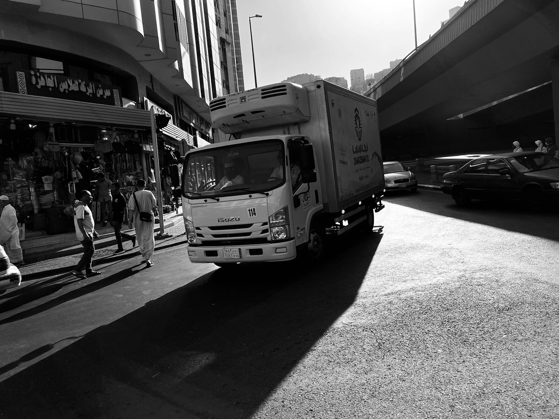 Monochrome image of a delivery truck navigating a bustling city street, highlighting urban life.