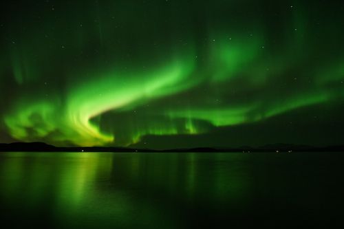Free Captivating view of the Northern Lights illuminating the night sky over a tranquil lake. Stock Photo