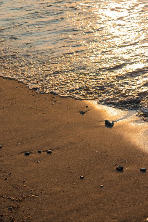 Free Golden sunlight bathes a sandy beach as gentle waves create a serene coastal scene. Stock Photo