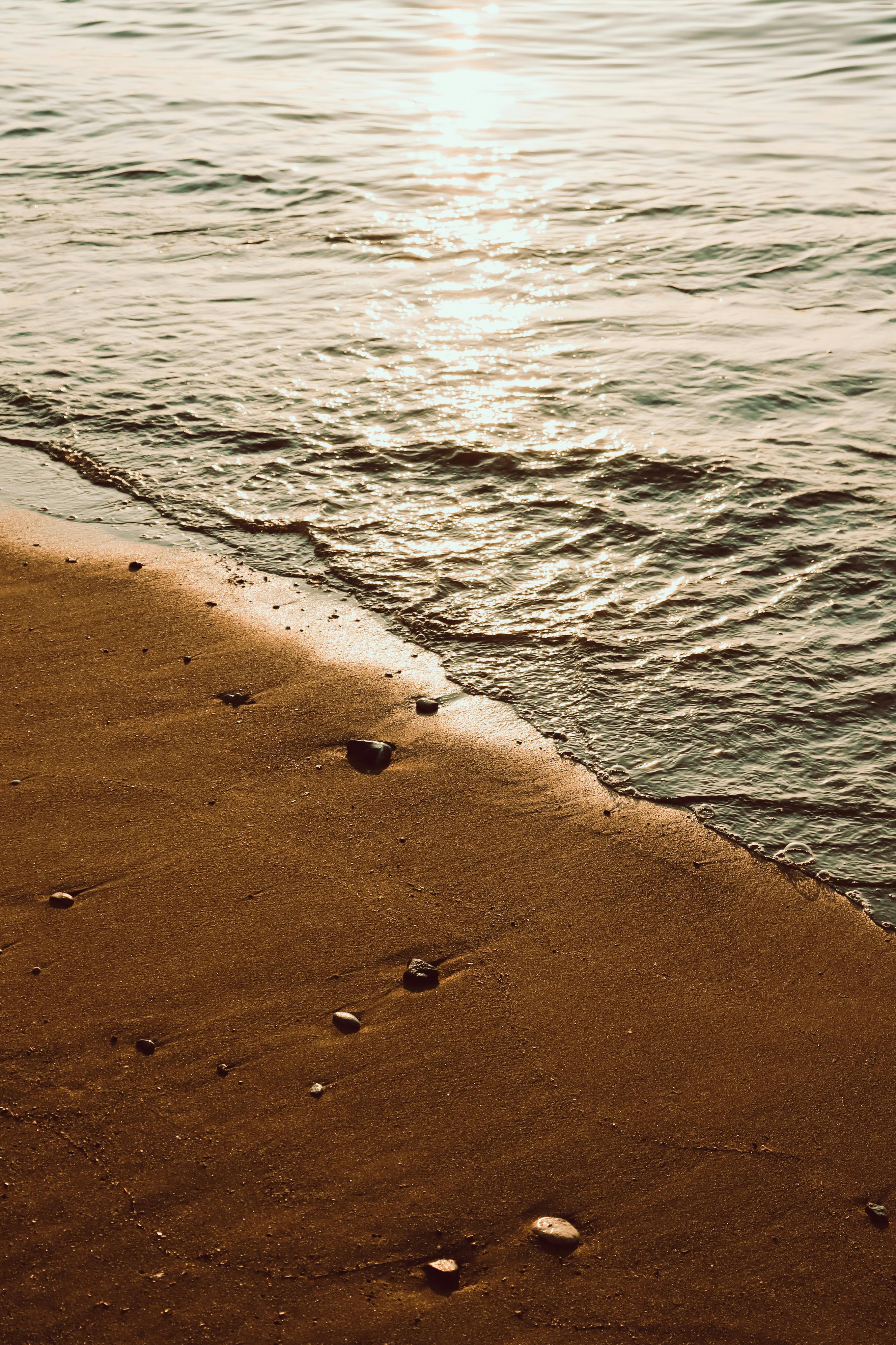 Peaceful golden beach at sunset with gentle waves and scattered pebbles.