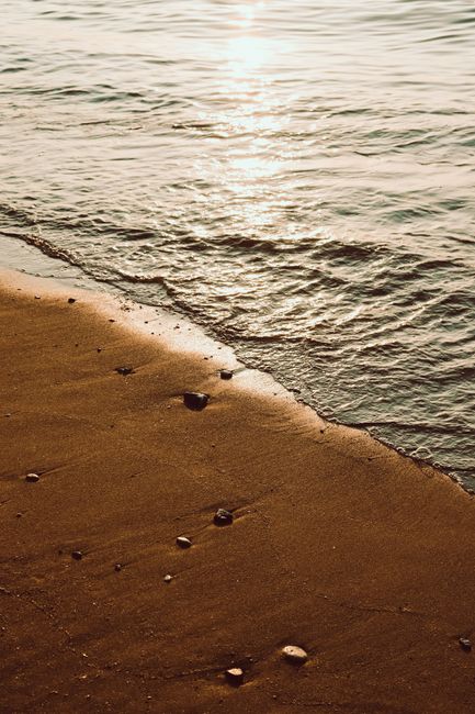 Peaceful golden beach at sunset with gentle waves and scattered pebbles.