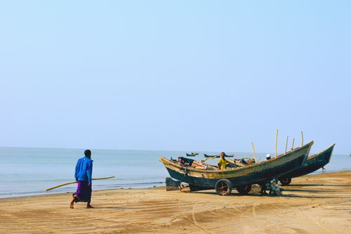 Free Men ready traditional boats for fishing on a sunlit beach, capturing a serene coastal scene. Stock Photo