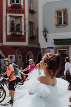 A bride enjoys ice cream in the picturesque streets of Hallstatt, Austria, amidst lively urban activity.