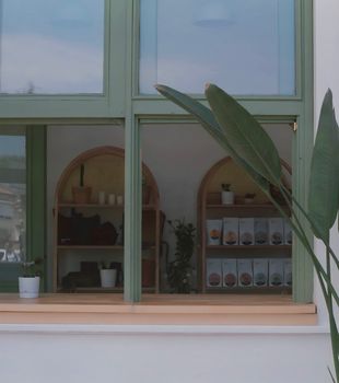 Exterior view of a café with a stylish green window frame and shelved products.