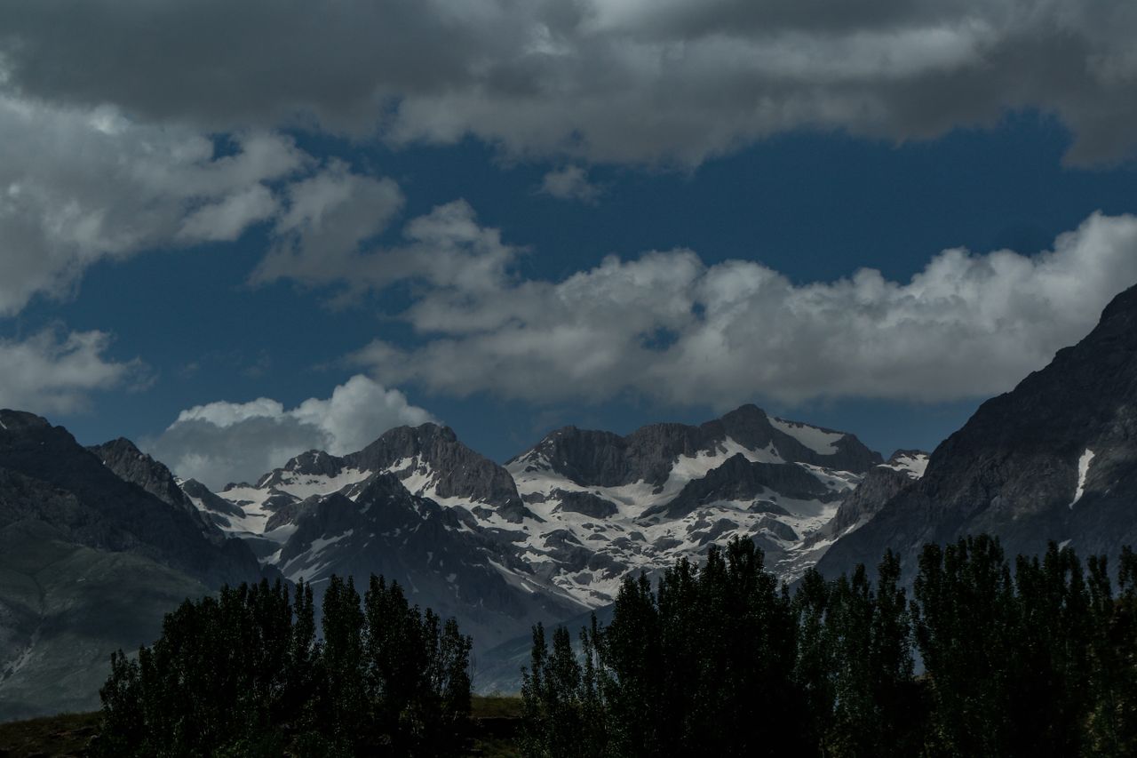a scenic view of snowcapped mountains with clouds trees and a valley b