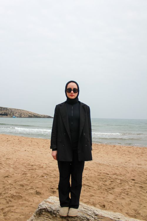 Free Young woman in black attire stands stylishly on a beach, exuding modern fashion vibes. Stock Photo