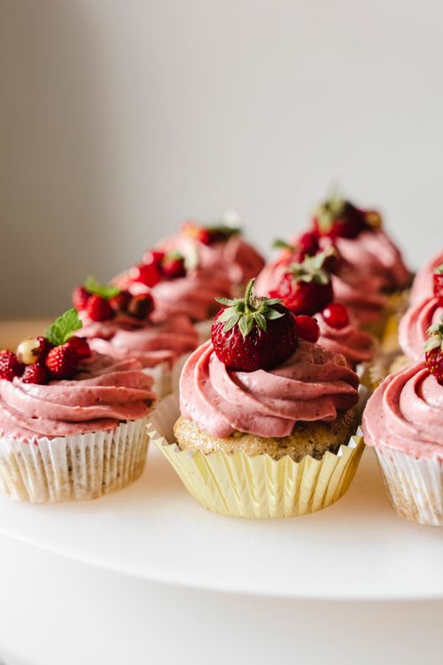 Free Close-up of cupcakes topped with strawberries and raspberries, showcasing pink cream frosting. Stock Photo