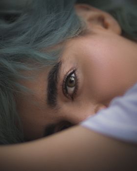 Close-up of a young woman with blue hair, showcasing her eye detail in a relaxed pose.
