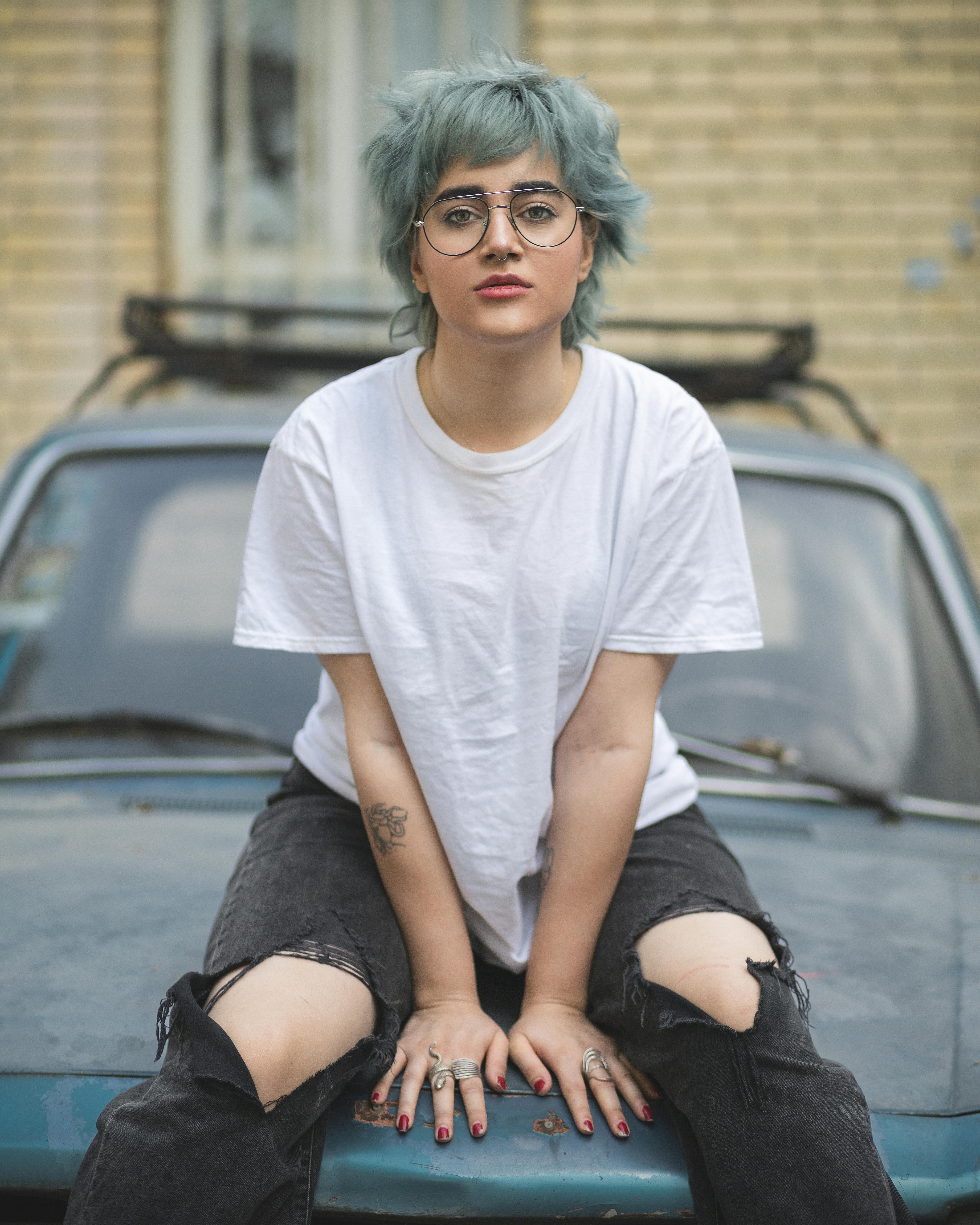 a woman with blue hair sitting on top of a car