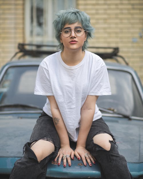 A woman with blue hair sitting on top of a car