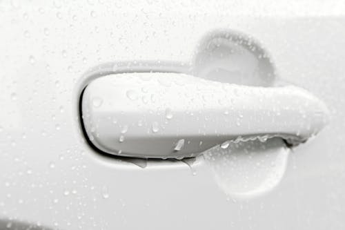 Door Handle of a White Car Dripping with Water